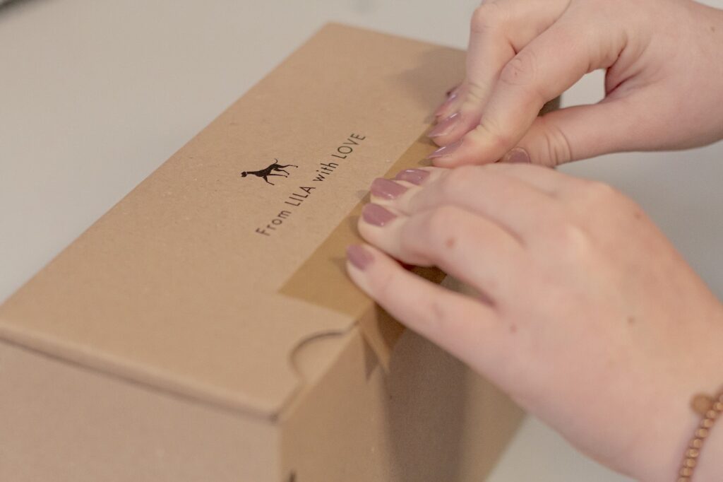 Paket mit der Aufschrift "From LILA with Love" wird von zwei Händen mit Klebeband verschlossen