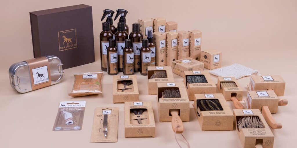 Große Auswahl stilvoll angeordneter Produkte in ähnlichem Design einer Pflege-Serie für Hunde aus Bürsten, Shampoos und weiteren Pflegemitteln in brauner Verpackung auf beigen Grund | LILA LOVES IT "Natürliche Pflege für Hunde"