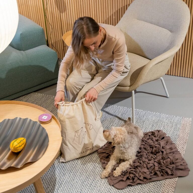 Frau packt Lila loves it Schnüffelteppich aus dem Beutel aus. Kleiner Hund liegt auf dem Schnüffelteppich und schnuppert am Beutel.