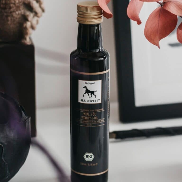 schwarze Flasche Lila Loves it Vital 5 Öl, im Hintergrund ein dekorativer roter Zweig und ein Rotkohl.