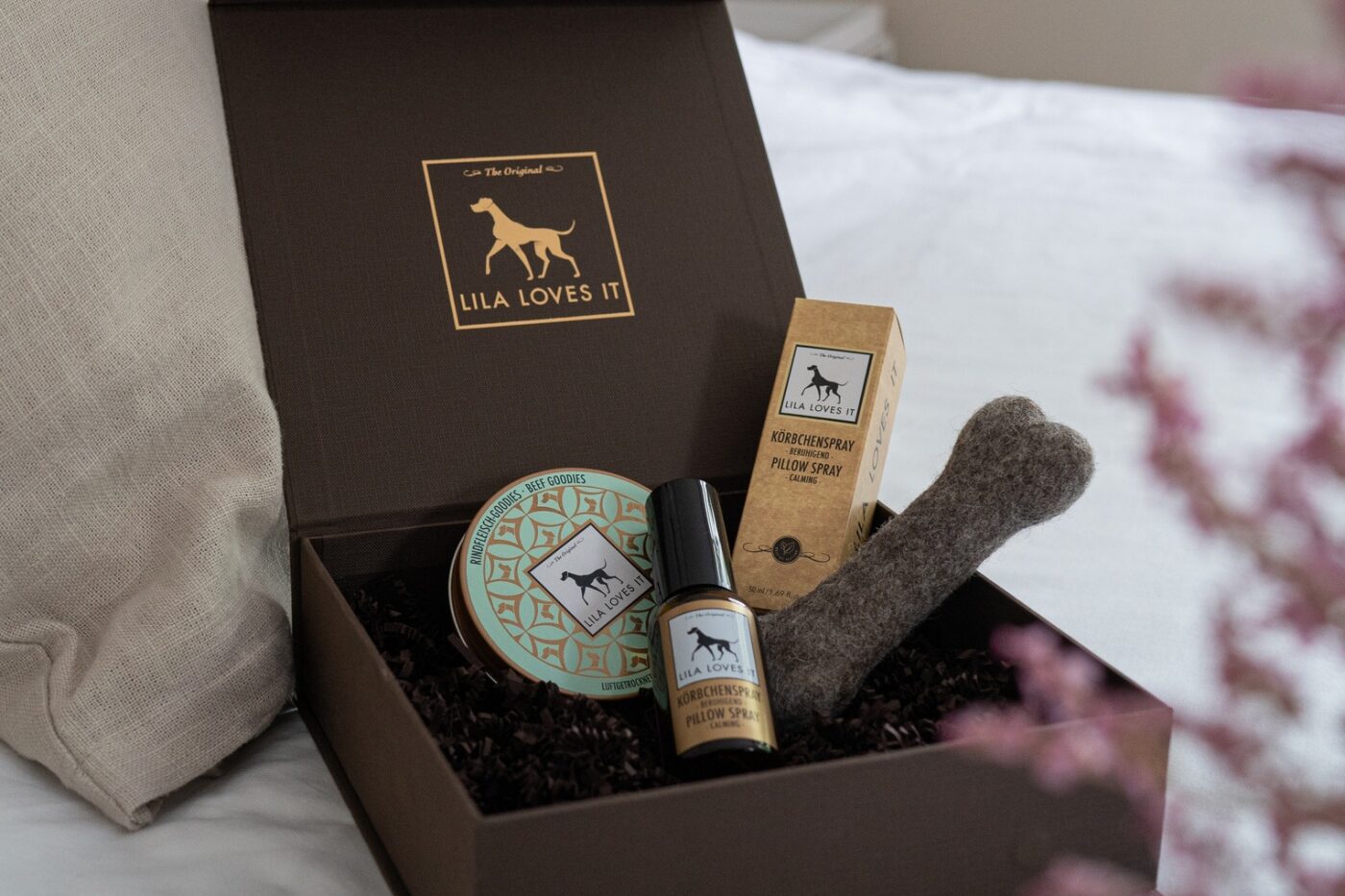 Elegenate braune Geschenkbox mit goldener Verziehrung auf einem frisch bezogenen Hotel Bett als Willkommensgeschenk für die Gäste und Ihren Hund | LILA LOVES IT "Hotel-Box: Rindfleisch-Goodies, Körbchenspray & Filzknochen für Hunde"